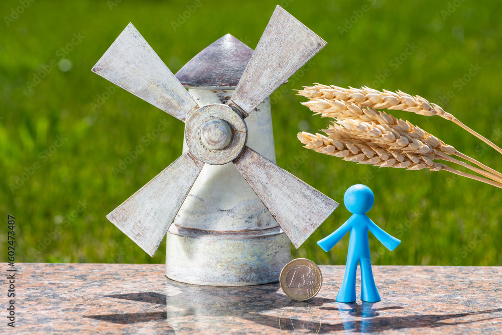 Ears of ripe wheat, a symbolic windmill, figurine of a man and a coin of denomination of 1 euro - obrazy, fototapety, plakaty 