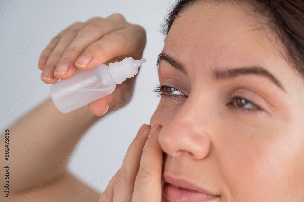 Caucasian woman dripping moisturizing drops into her eyes. Caucasian woman dripping moisturizing drops into her eyes.