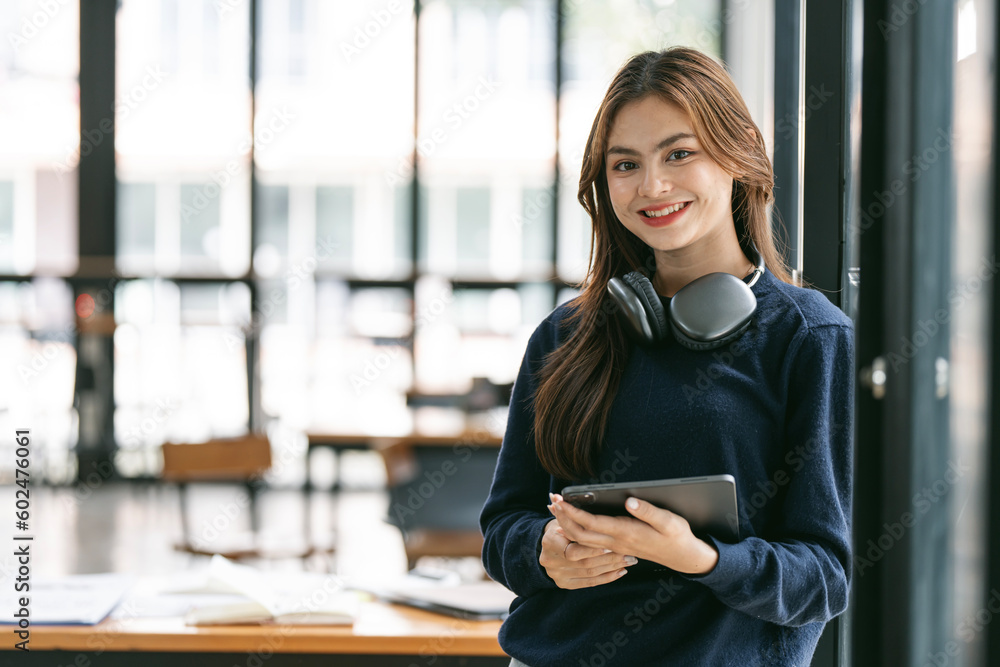 Obraz premium Young Beautiful university student with headphone holding tablet standing in co-workspace.