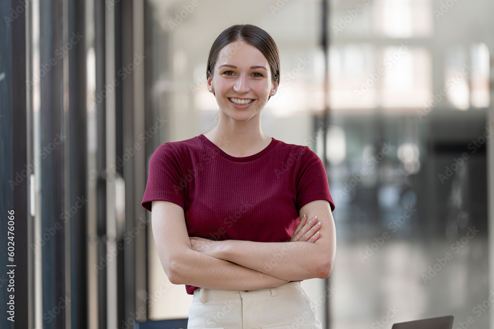 Portrait of young smiling woman looking at camera with crossed arms. Happy girl standing in creative office. Portrait of young smiling woman looking at camera with crossed arms. Happy girl standing in creative office.
