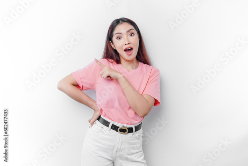 Shocked Asian woman wearing pink t-shirt, pointing at the copy space on beside her, isolated by white background © Reezky