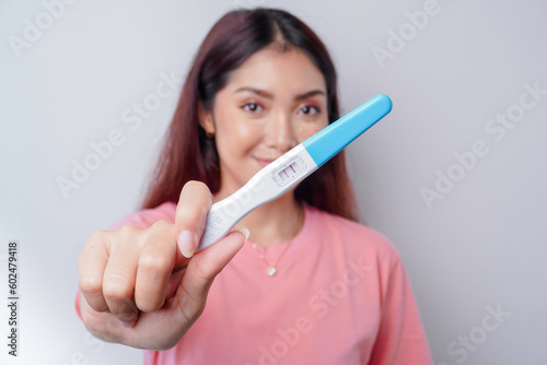 Happy young woman wearing pink t-shirt showing her pregnancy test, isolated on white background, pregnancy concept