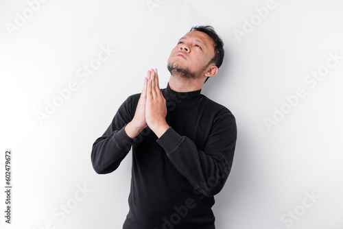 Religious Asian man wearing a black shirt praying to God, isolated by a white background photo