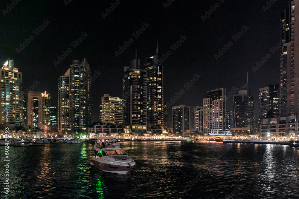 Night view from the promenade of Dubai Marina with illuminated skyscrapers, a water channel, yachts and ships in Dubai city, United Arab Emirates