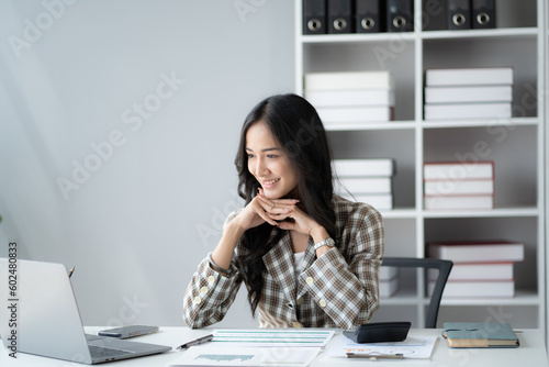 Charming young Asian businesswoman working with laptop computer while sitting at the office desk.