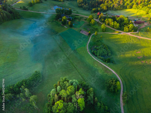 Rising Above the Beauty: Aerial View of Serene Green Pastures, Trees and Gravel Road During Sunrise with Drone in Northern Europe