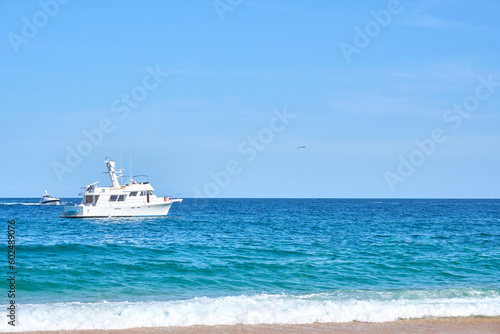 white yacht in the pacific ocean, waves at the shore and golden sand, baja california sur, los cabos, mexico.