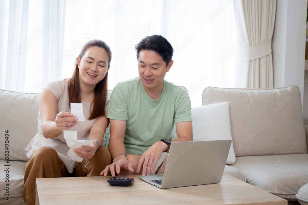 Happy family with couple sitting on sofa calculate finance and expenses of household together in living room at home, man and woman checking bill and invoice for cost, lifestyles and saving concept. Happy family with couple sitting on sofa calculate finance and expenses of household together in living room at home, man and woman checking bill and invoice for cost, lifestyles and saving concept.