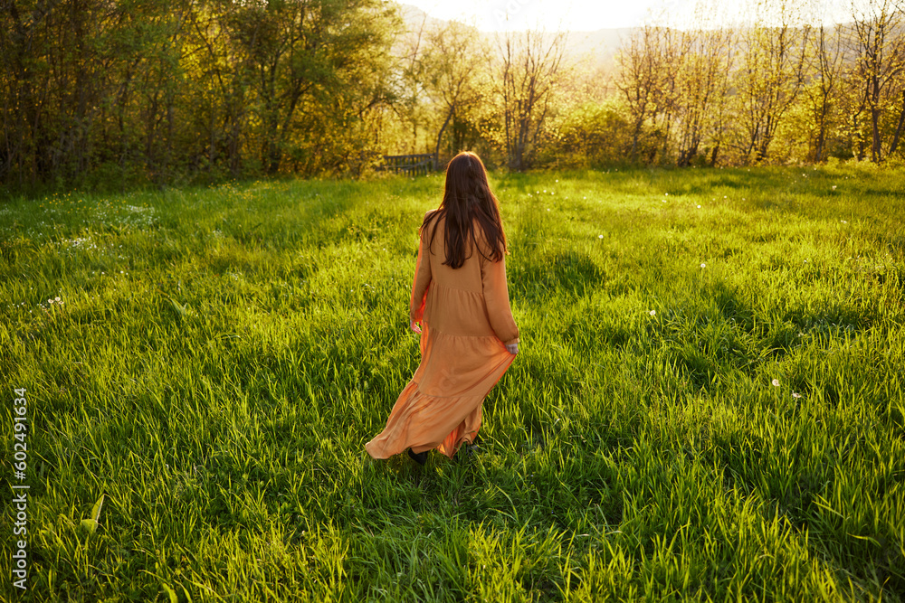 an attractive, slender, red-haired woman walks through a field during sunset, in a long orange dress enjoying unity with nature and relaxation holding the edge of her clothes an attractive, slender, red-haired woman walks through a field during sunset, in a long orange dress enjoying unity with nature and relaxation holding the edge of her clothes