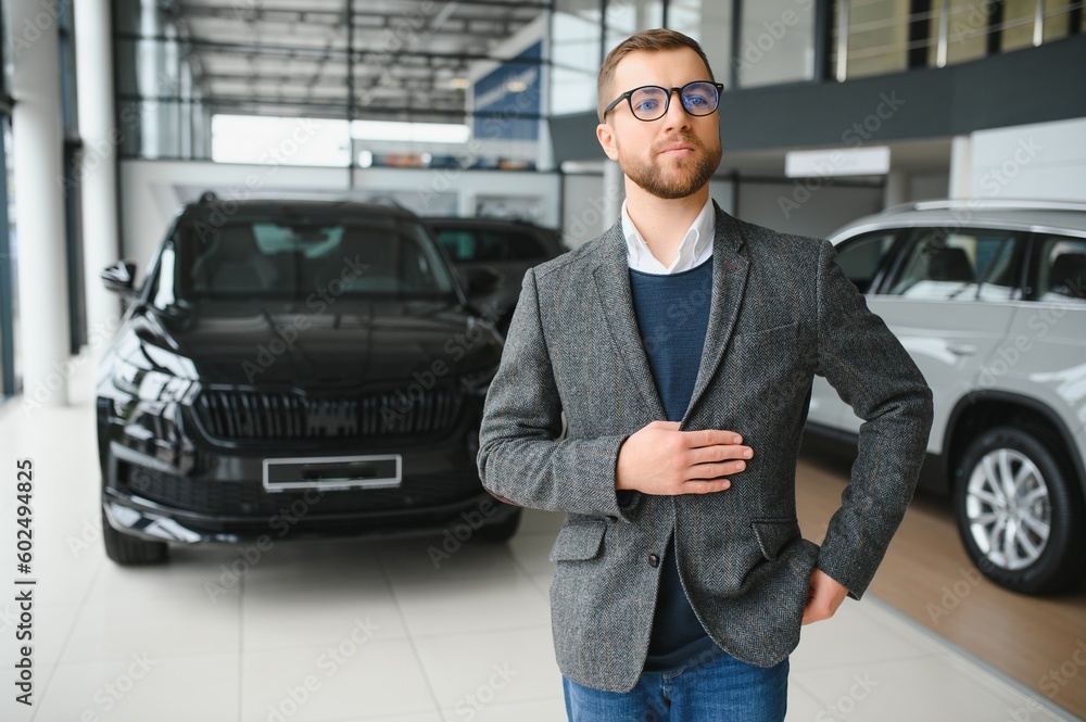 Portrait of a handsome salesman in the suit standing near the car in the showroom Portrait of a handsome salesman in the suit standing near the car in the showroom