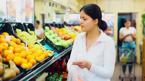 Young woman shopping and choosing local juicy mandarins in hypermarket. High quality 4k footage photo