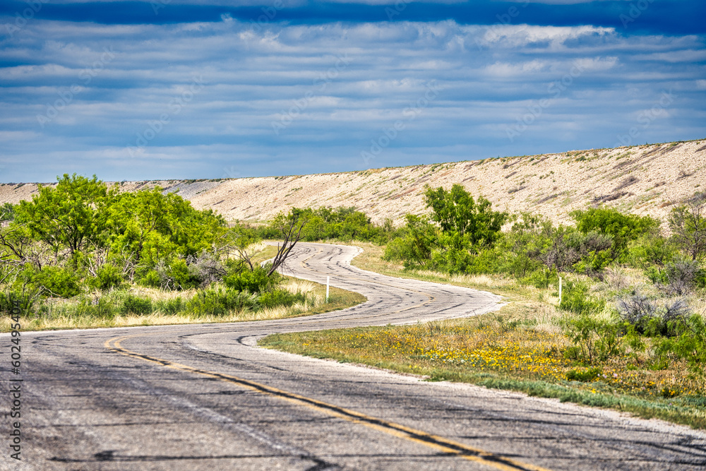A tranquil landscape of a cloud-filled sky over an expansive dam, tree-lined roads and plants in San Angelo State Park, Texas. A tranquil landscape of a cloud-filled sky over an expansive dam, tree-lined roads and plants in San Angelo State Park, Texas.