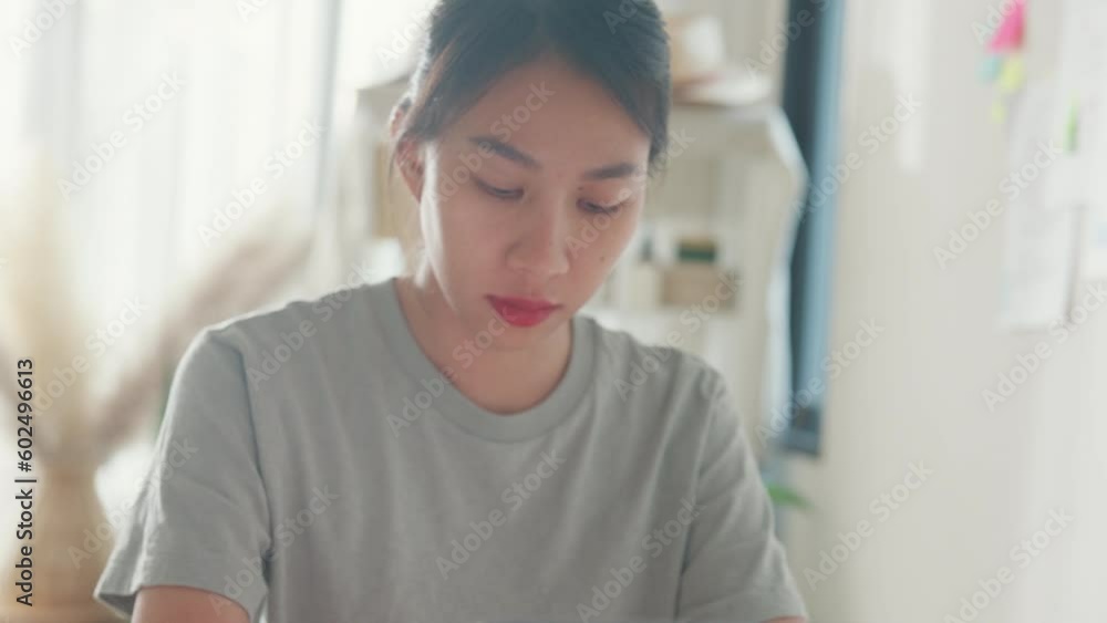 Close-up Young Asia girl IT development programmer typing on keyboard coding programming fixing data code on laptop computer screen follow code plan in tablet and paperwork on table at house office. Close-up Young Asia girl IT development programmer typing on keyboard coding programming fixing data code on laptop computer screen follow code plan in tablet and paperwork on table at house office.