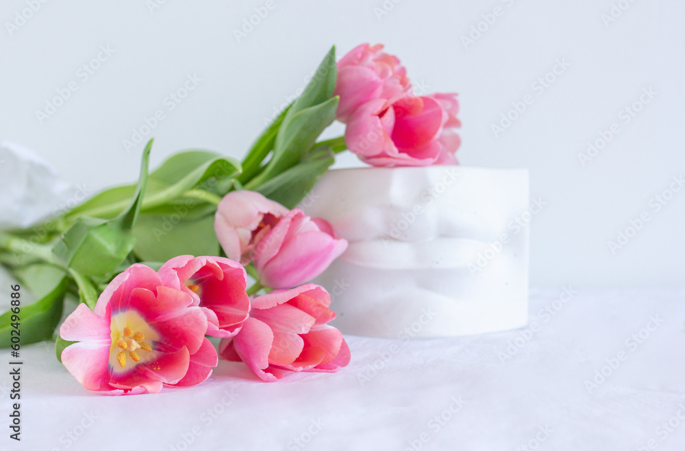 Pink tulips bouquet and plaster statue of lips lying on white wrinkled blanket background copy space