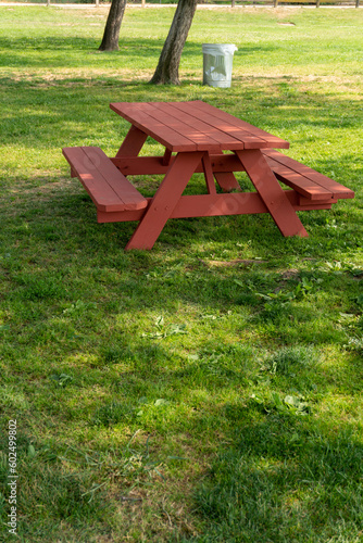 Picnic area with red table, trees and trash can in the park