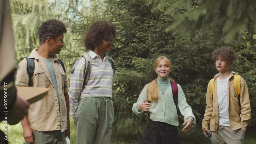 Medium shot of group of multiracial kids chatting during school one day trip to summer forest with ranger Medium shot of group of multiracial kids chatting during school one day trip to summer forest with ranger