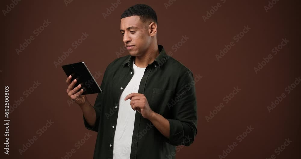 Young african american man using tablet pc standing over brown studio background Young african american man using tablet pc standing over brown studio background
