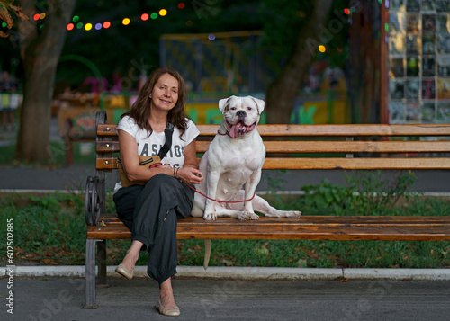 Pretty woman sits on a bench in a city park with her American Bulldog breed dog