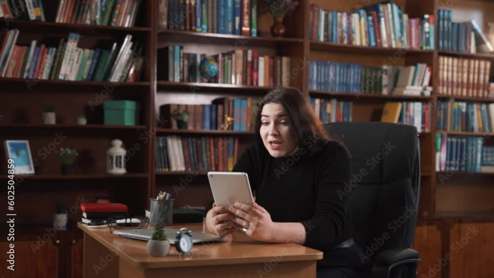 The girl is sitting at a desk with a tablet in her hands. She is watching a video very emotionally and cheering for someone. In the end, she expresses satisfaction and victory with her emotions. The girl is sitting at a desk with a tablet in her hands. She is watching a video very emotionally and cheering for someone. In the end, she expresses satisfaction and victory with her emotions.