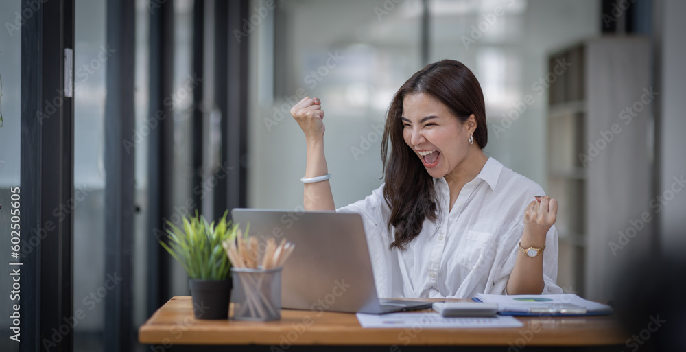 Excited Happy Asian young woman using phone and laptop sitting on a desk office in the day at office Excited Happy Asian young woman using phone and laptop sitting on a desk office in the day at office