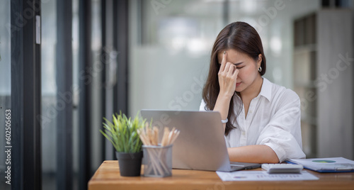 Portrait of tired young business Asian woman work with documents tax laptop computer in office. Sad, unhappy, Worried, Depression, or employee life stress concept 