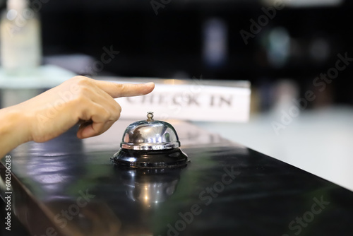 Closeup of a hand ringing a silver service bell at the hotel reception desk