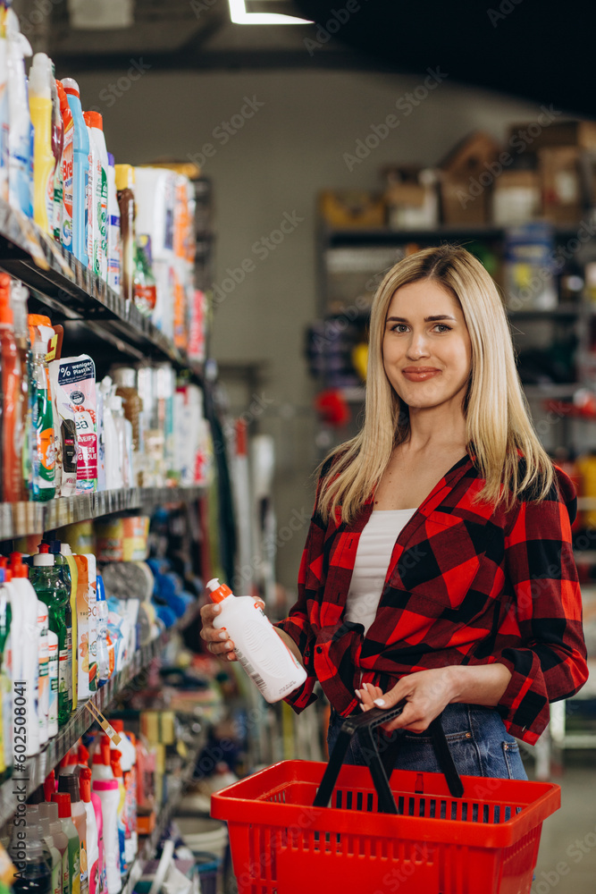 Fototapeta premium Interested young woman making purchases in household chemicals store, reading labels on bottles.