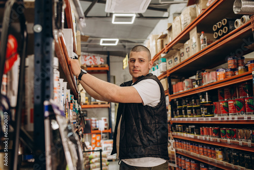 Caucasian consultant in uniform at hardware store. Male standing next to shelves with tools at store.