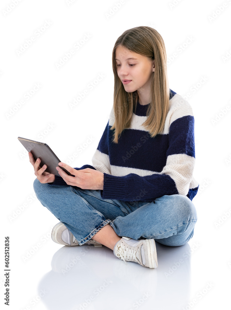 Obraz premium Full length portrait of pretty girl sitting on floor working on laptop pc computer isolated on white background. Fourteen year old teenager in striped sweater reading and posing in studio.