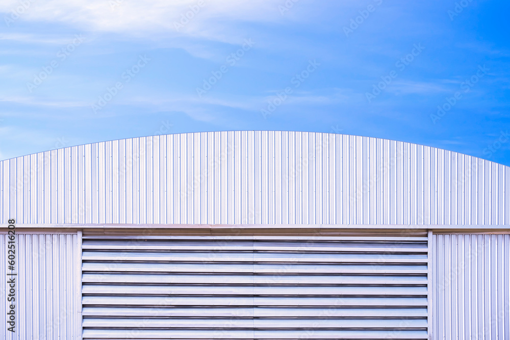 Aluminium louver on corrugated steel wall of warehouse building with curve metal roof against blue sky background Aluminium louver on corrugated steel wall of warehouse building with curve metal roof against blue sky background