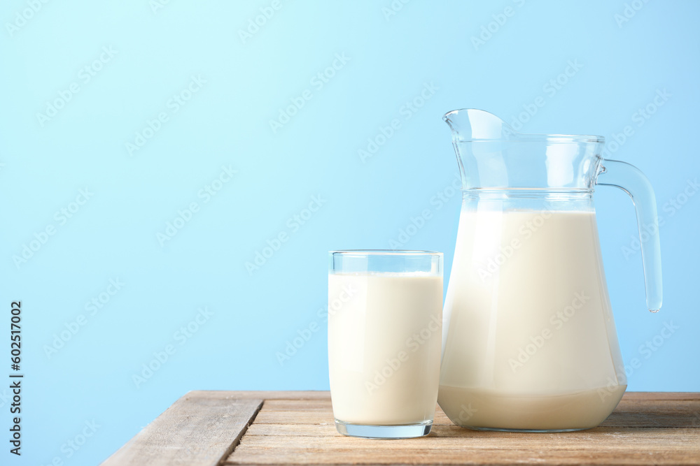 Glass and pitcher of fresh milk on wooden table with light blue background. - obrazy, fototapety, plakaty 