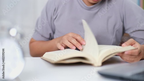 Closeup image of Asian woman sitting at a table reading a book in the living room.