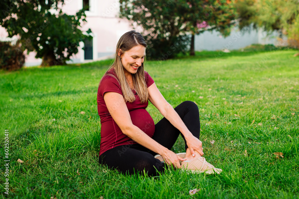 Smiling pregnant woman wearing shoe sitting on grass in lawn Smiling pregnant woman wearing shoe sitting on grass in lawn