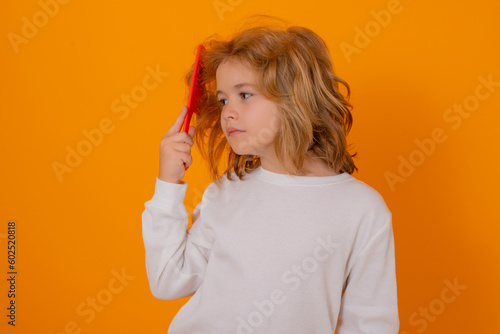 Portrait of child combing hair with comb on yellow studio background. Conditioner and shampoo for kids hair. Child with tangled blonde long hair tries to comb it. Hair portrait kid with a comb.