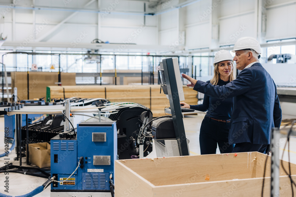 Manager explaining machine to colleague standing in factory Manager explaining machine to colleague standing in factory