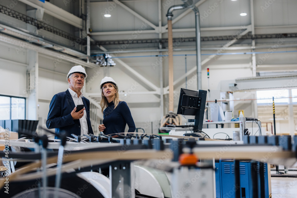 Businessman and colleague standing near machine in factory Businessman and colleague standing near machine in factory