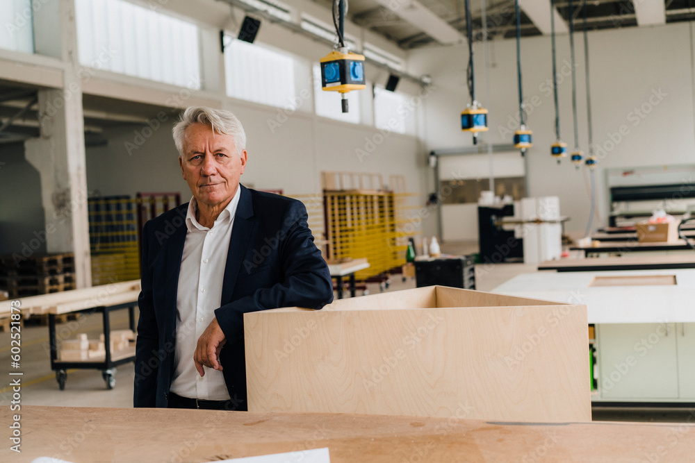 Businessman leaning on wooden structure in factory Businessman leaning on wooden structure in factory