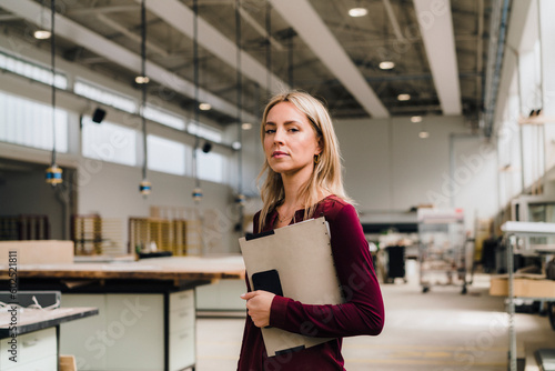 Confident businesswoman with blond hair holding file in factory photo