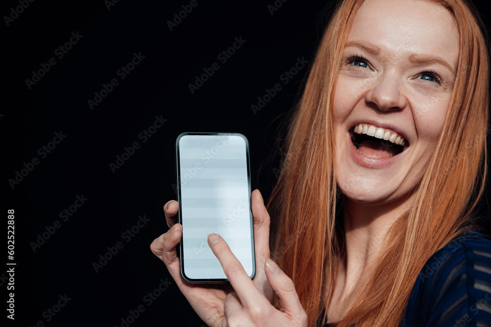 Young woman laughing and holding smart phone against black background Young woman laughing and holding smart phone against black background