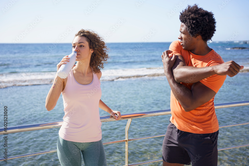 Man exercising with girlfriend drinking water by railing in coastal area Man exercising with girlfriend drinking water by railing in coastal area