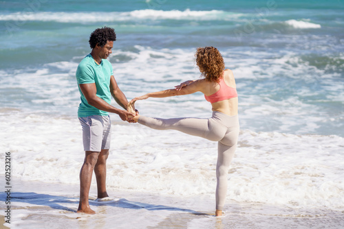 Man assisting girfriend standing on one leg at seashore photo