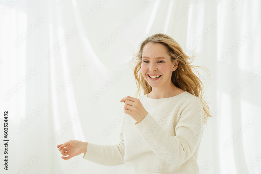 Smiling woman with blond hair dancing in front of white translucent curtain Smiling woman with blond hair dancing in front of white translucent curtain