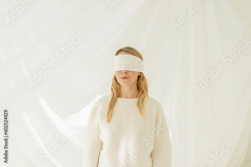 Blond woman with blindfold standing in front of translucent curtain