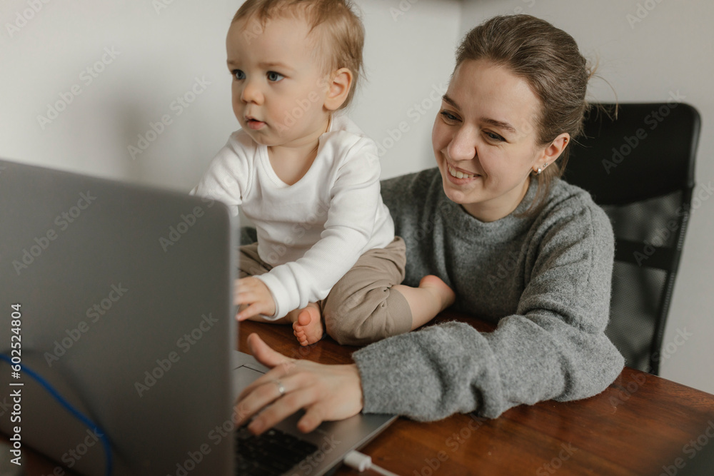 Smiling mother working on laptop with baby boy at home office Smiling mother working on laptop with baby boy at home office
