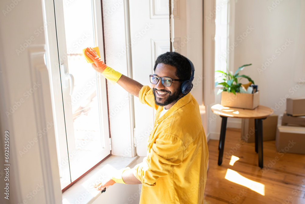 Smiling man enjoying music with headphones and cleaning window Smiling man enjoying music with headphones and cleaning window