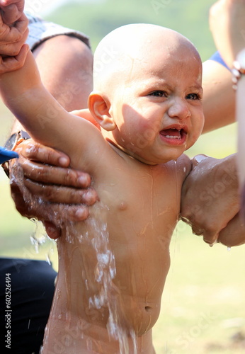 Toddler baby boy having bath after getting mundan, balding ceremony outside, baby is crying due to unexpected action done with him. Mundan is famous in Indian Hindu religion photo