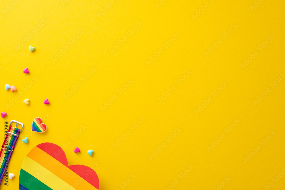 A top view flat lay of parade symbolic accessories, including wristlet, badge, hearts, rainbow card, on yellow backdrop with empty space for text or ad, celebrating the theme of Pride and inclusivity - obrazy, fototapety, plakaty 