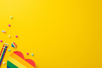 A top view flat lay of parade symbolic accessories, including wristlet, badge, hearts, rainbow card, on yellow backdrop with empty space for text or ad, celebrating the theme of Pride and inclusivity
