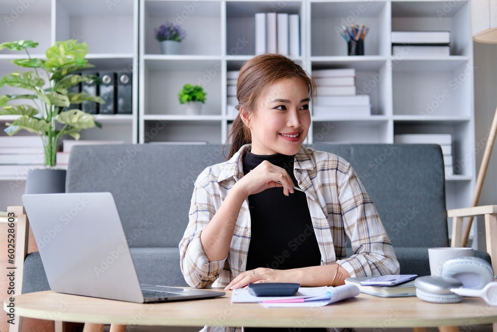 Young Asian female student sitting taking notes and using laptop computer at table. Young Asian female student sitting taking notes and using laptop computer at table.