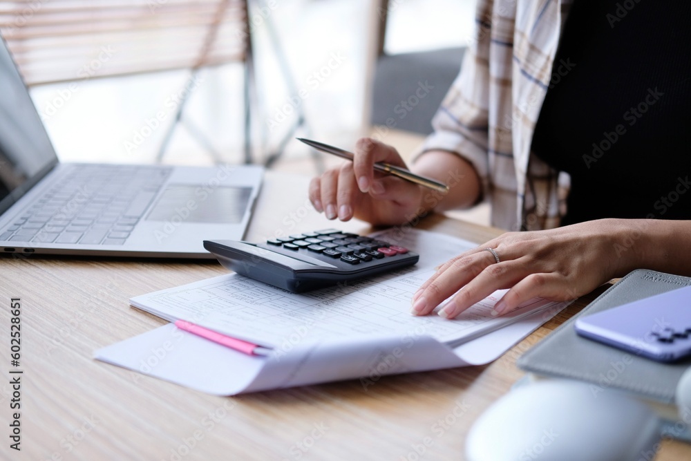 Fototapeta premium Businesswomen hands working with finances about cost and calculator and laptop with tablet, smartphone at office in morning light